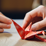 **Image Prompt:** Close-up shot of hands meticulously crafting a delicate origami crane from vibrant washi paper, soft, diffused lighting, shallow depth of field, focus on the intricate folds, background blurred with subtle Japanese patterns.